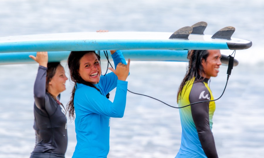 Guests laughing while carrying a surfboard during the beginner course
